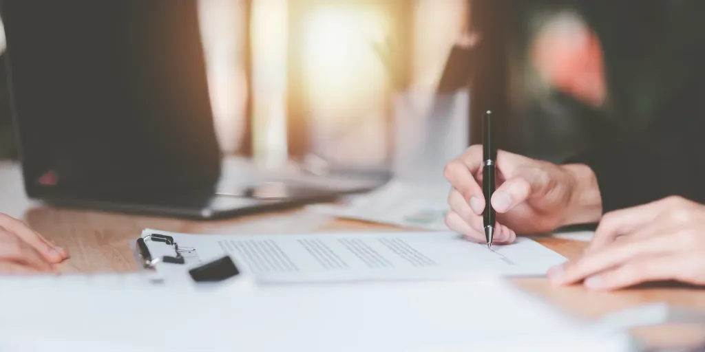 Deux personnes signant un document sur une table, devant un ordinateur portable